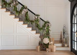 Festive Christmas Decorations adorning a Staircase Railing in Modern Home. Garland, Holiday Trees and wrapped presents in Tan Paper with Silver Bell Accents